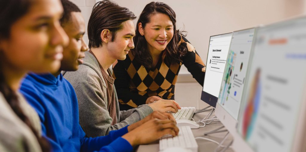 a teacher assisting a student on a classroom desktop smiling